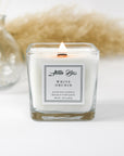 A white orchid candle with a clear glass container, featuring a label with the brand name 'Abeille Bliss' and the scent 'White Orchid'.