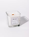 A white candle with a label that reads 'Strawberry', placed in a clear glass container.