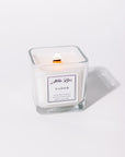 A white candle with a label that reads 'NADOR', placed in a clear glass holder.
