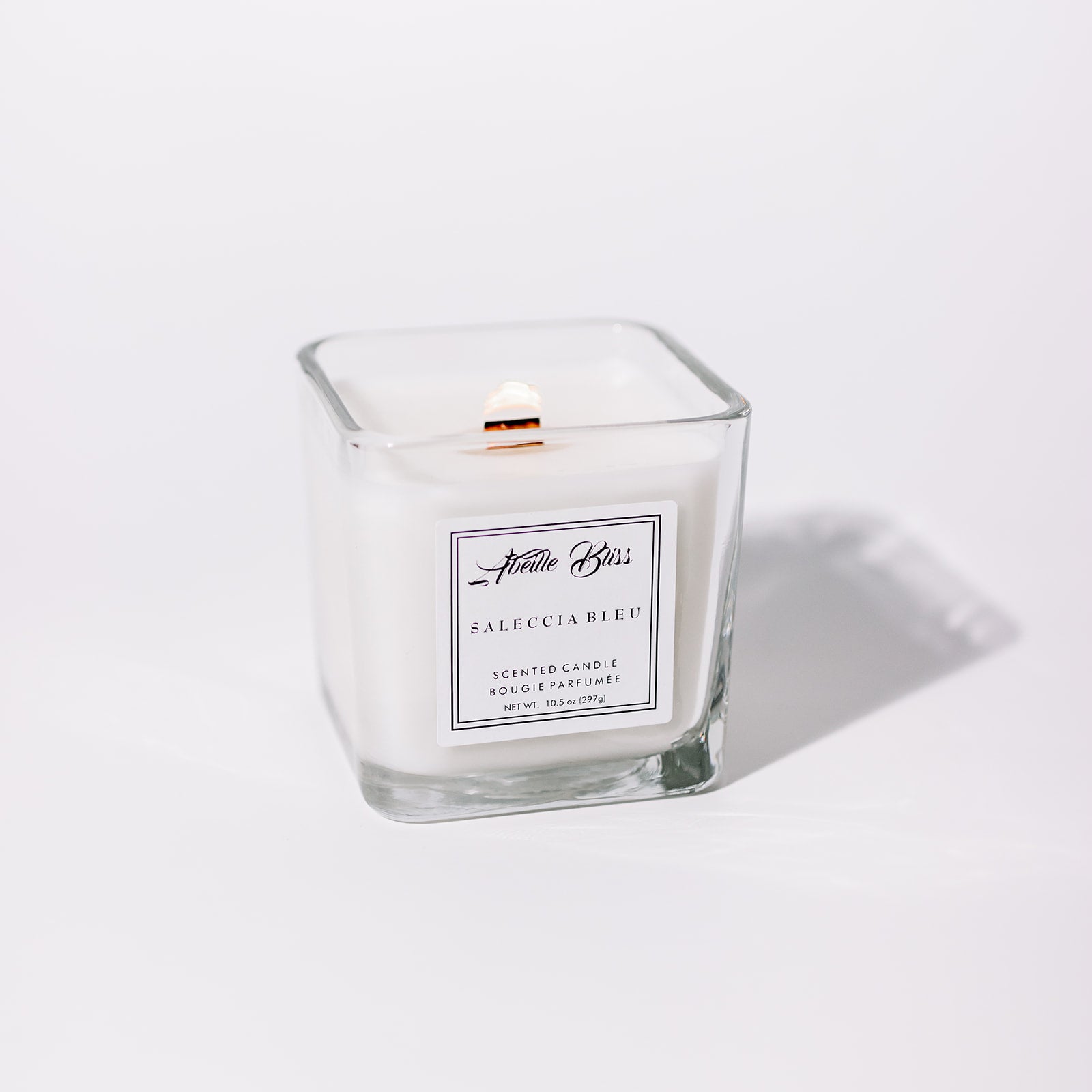 A white candle with a label that reads 'Saleccia Bleu'. It is contained in a clear glass jar and appears to have a single wood wick.