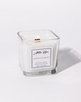 A white candle with a label that reads 'Saleccia Bleu'. It is contained in a clear glass jar and appears to have a single wood wick.