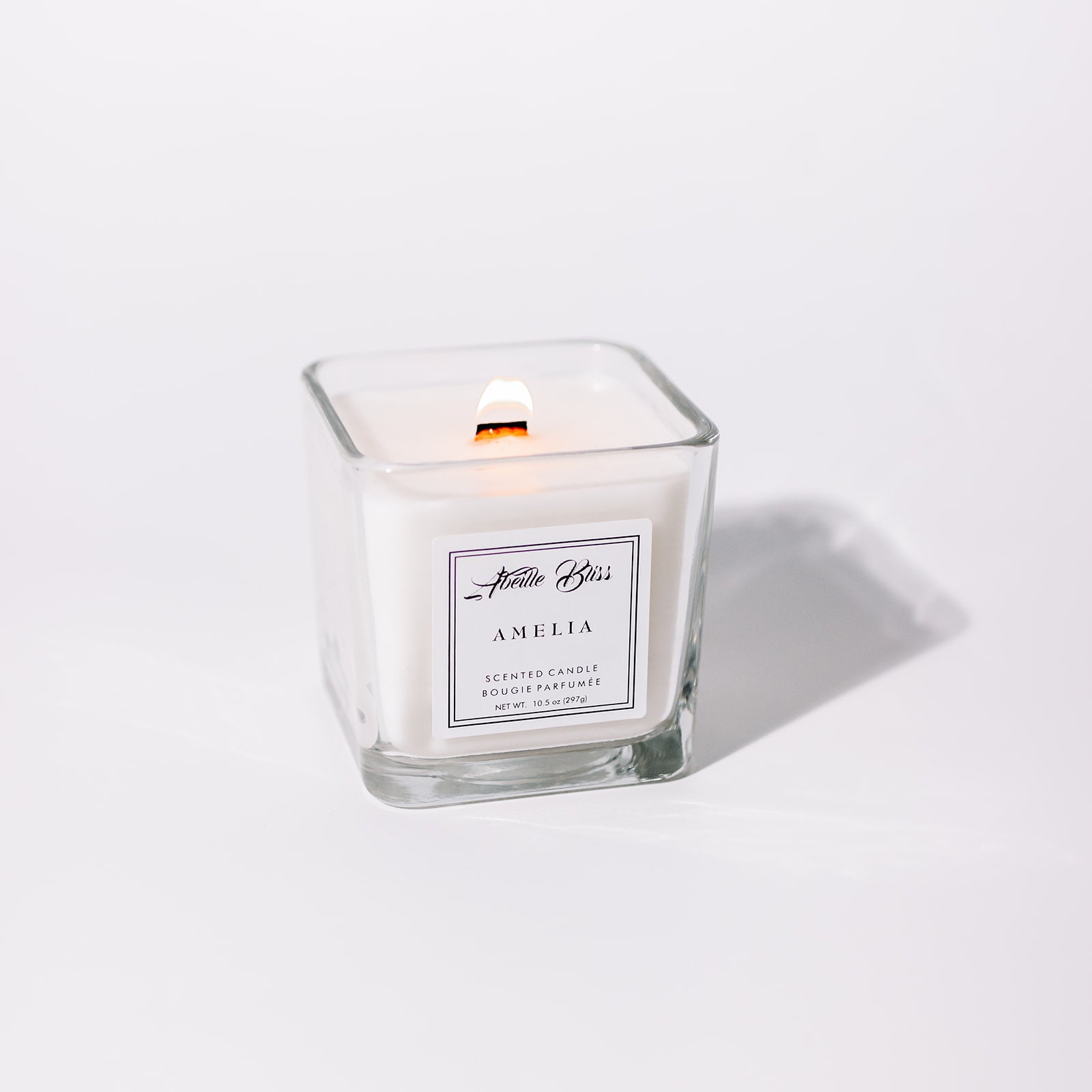 A white candle named 'Amelia' in a clear glass holder with a label in front.