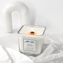 A white orchid scented candle with a label that reads 'White Orchid'. The candle is placed on a white, textured surface and has a wood wick.